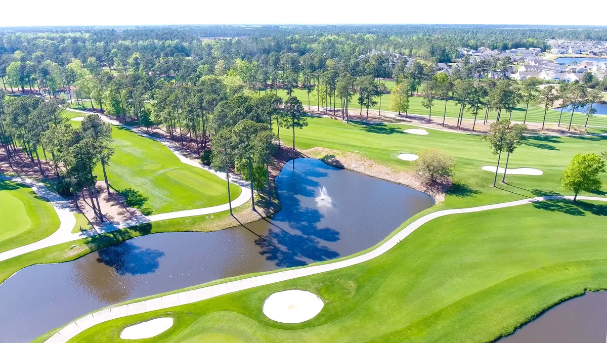 A peaceful scene on the lush golf course, focusing on a pond, rolling fairways, and mature trees. Early morning or sunset light creates a serene atmosphere, with golf holes in the foreground emphasizing the recreational appeal.
