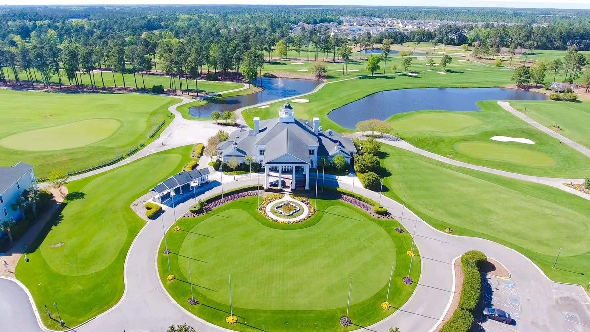 An elegant exterior shot of the clubhouse, surrounded by landscaped gardens, golf courses, and water features. The clubhouse stands as a central social hub, offering spaces for dining, events, and relaxation, with beautiful golf course views underscoring the luxury setting.