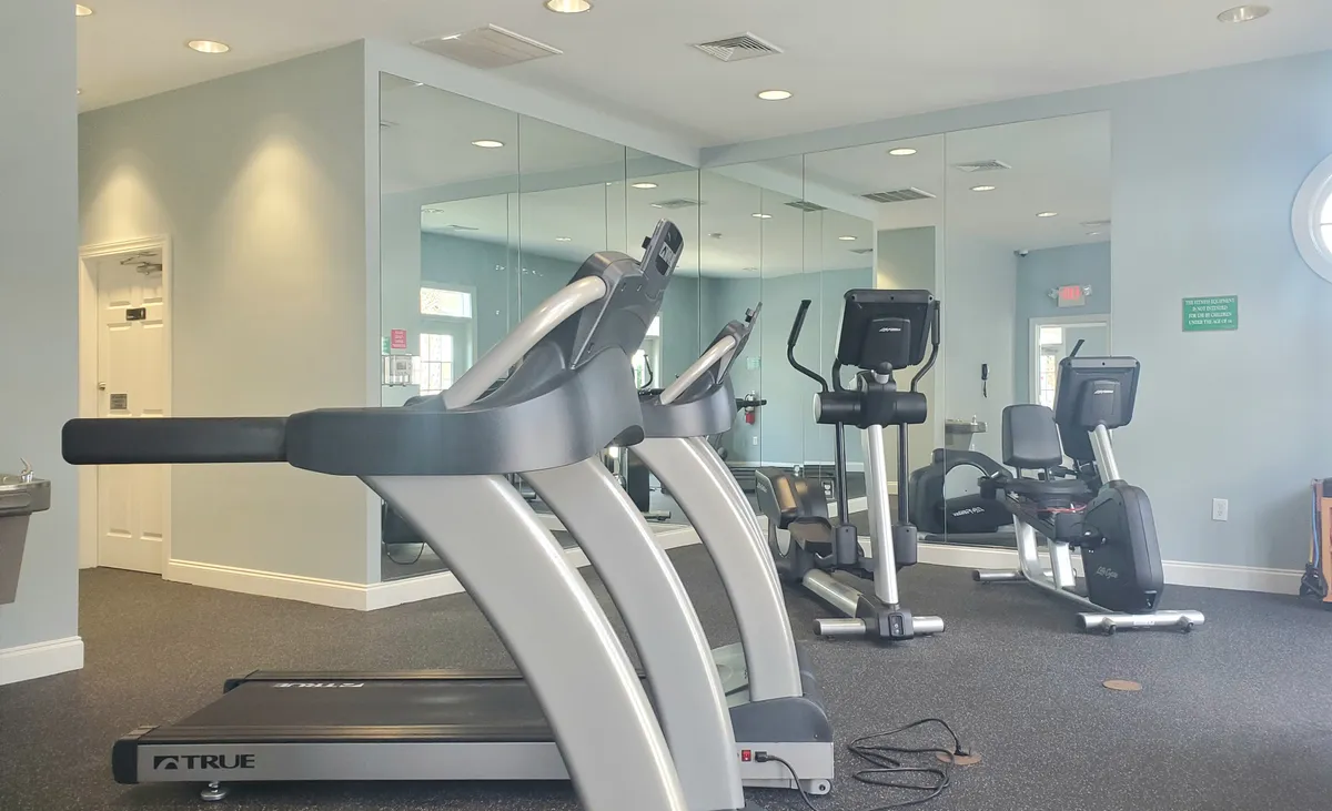 A bright and modern fitness center is shown, with advanced exercise equipment such as treadmills and ellipticals positioned in front of a mirrored wall. The space is inviting for couples looking to work out together and maintain wellness during their stay.