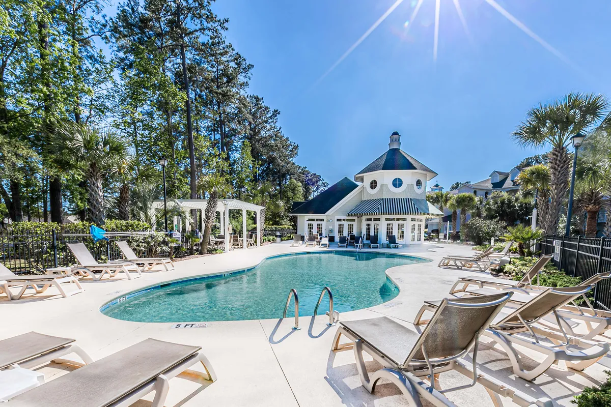 A vibrant exterior view of the community swimming pool, complete with a view of the clubhouse, lounge chairs, and lush surrounding greenery. The scene exudes a vacation-like atmosphere, showing the pool as a hub for swimming, sunbathing, and social gatherings, with inviting spaces for residents to relax and unwind.