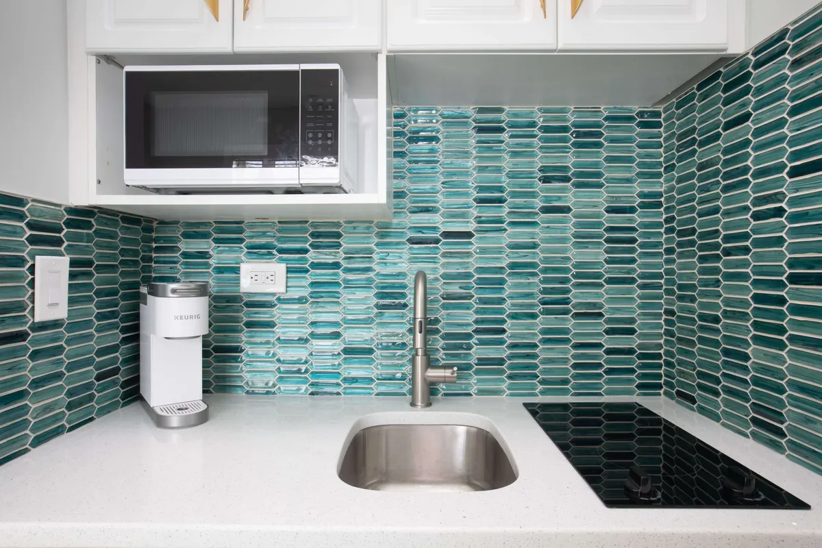 A contemporary kitchenette featuring a textured backsplash, sink, cooktop, microwave, and coffee machine. The setup is perfect for quick breakfasts, meal prep, or brewing a comforting cup of coffee at any hour.
